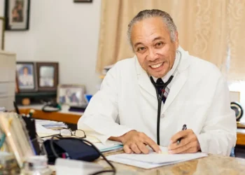 Dr. Martin Didier, a distinguished Saint Lucian medical professional, smiling and seated at his desk in a white lab coat, showcasing his commitment to healthcare.
