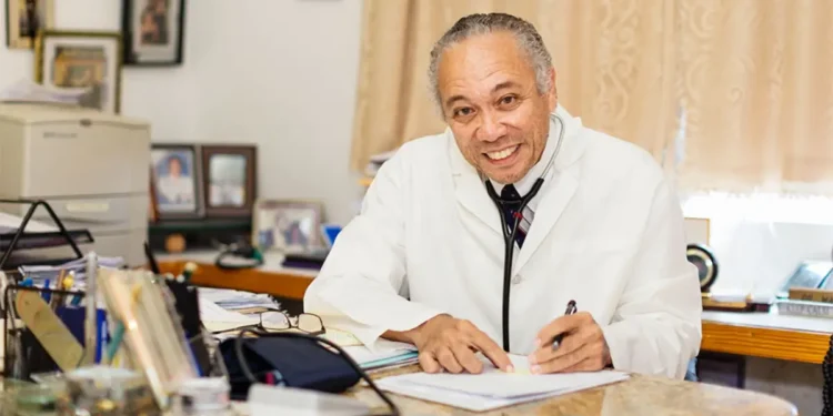 Dr. Martin Didier, a distinguished Saint Lucian medical professional, smiling and seated at his desk in a white lab coat, showcasing his commitment to healthcare.
