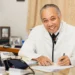 Dr. Martin Didier, a distinguished Saint Lucian medical professional, smiling and seated at his desk in a white lab coat, showcasing his commitment to healthcare.