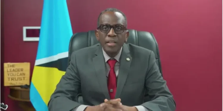 Philip J. Pierre speaks during the third anniversary of his party, against a dirty red background, highlighting the St. Lucia Healthcare Crisis