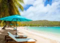Tourists leisurely strolling on a white sand beach, enjoying the beautiful sunshine at the Caribbean Tourism Conference 2024 in the Cayman Islands.