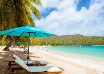 Tourists leisurely strolling on a white sand beach, enjoying the beautiful sunshine at the Caribbean Tourism Conference 2024 in the Cayman Islands.
