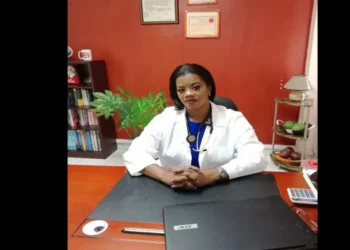 Dr. Merle Clarke in a lab coat, sitting at her desk, addressing the Saint Lucia healthcare crisis in a detailed letter to the OKEU Board.