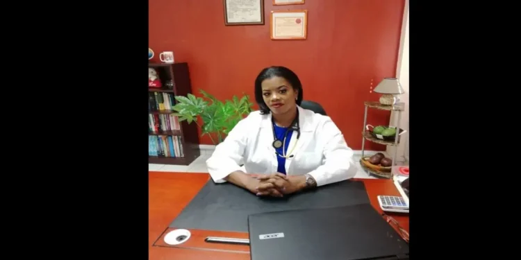 Dr. Merle Clarke in a lab coat, sitting at her desk, addressing the Saint Lucia healthcare crisis in a detailed letter to the OKEU Board.