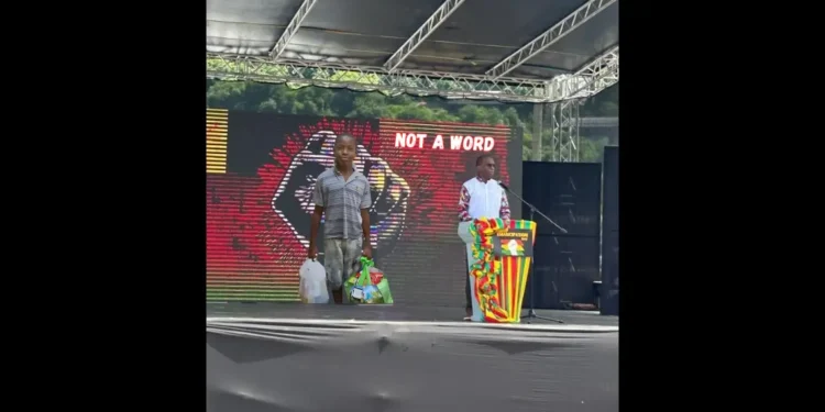 Saint Lucia government silence illustrated as Philip J. Pierre speaks at a podium on Emancipation Day with a backdrop of Young Melchizedek Tixcy holding grocery bags reading Not a Word.