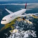 A Delta airplane flying over snow-capped mountains and valleys, illustrating the story of a stowaway on a Delta flight to Paris.