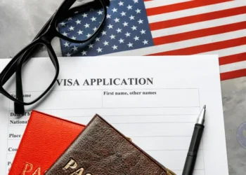 A US visa application form with a pen, passport, glasses, and an American flag, representing the US Visa Waiver Program process.