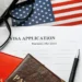 A US visa application form with a pen, passport, glasses, and an American flag, representing the US Visa Waiver Program process.