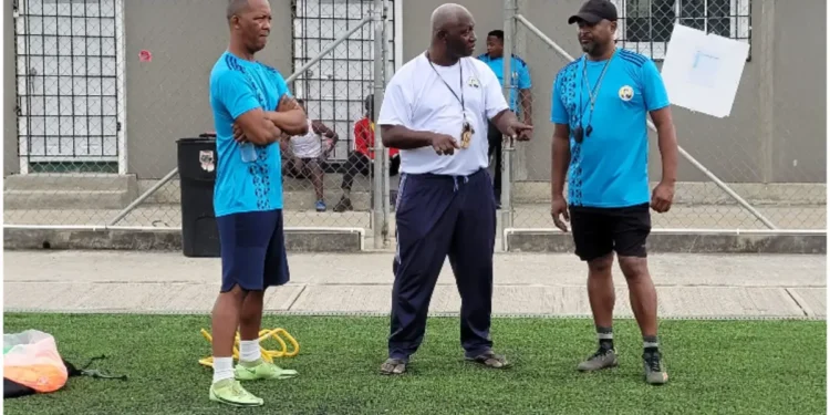 Emmanuel Bellas, legendary Vieux Fort football coach, in a white shirt during a coaching session, sharing his expertise and leadership.