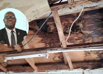 Castries Polyclinic roof leak showing water-damaged plywood with an overlay of Health Minister Moses Jn Baptiste addressing the issue.