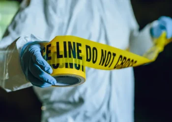 Stock image of a crime scene investigator unrolling yellow tape, symbolizing the investigation into the Delcer Stabbing Incident in Saint Lucia.