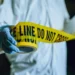 Stock image of a crime scene investigator unrolling yellow tape, symbolizing the investigation into the Delcer Stabbing Incident in Saint Lucia.