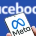 A smartphone displaying the Meta logo with a blurred Facebook logo in the background, symbolizing the Meta policy shift toward free expression and community-driven moderation.
