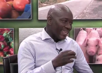 Alfred Prospere Faces Backlash as he speaks with photos of pigs and vegetables in the background.