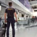 Back view of a security officer with a police dog at an airport terminal, representing enhanced safety measures and 2025 travel requirements.