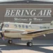 A Bering Air Cessna 208B Grand Caravan parked in front of a hangar with Welcome to Nome signage. The aircraft is similar to the missing Alaska plane carrying 10 people.