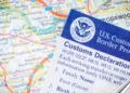 A U.S. Customs and Border Protection customs declaration form placed over a map, representing immigration enforcement as the Trump administration mandates alien registration.