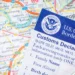 A U.S. Customs and Border Protection customs declaration form placed over a map, representing immigration enforcement as the Trump administration mandates alien registration.