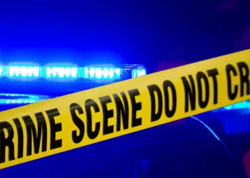 Crime scene with police lights flashing behind yellow tape reading 'CRIME SCENE DO NOT CROSS,' representing the report of a gruesome homicide in Aux Leon Dennery.