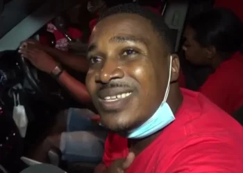 Jeremiah Norbert at a 2021 election motorcade, engaging with supporters in a red shirt and mask.