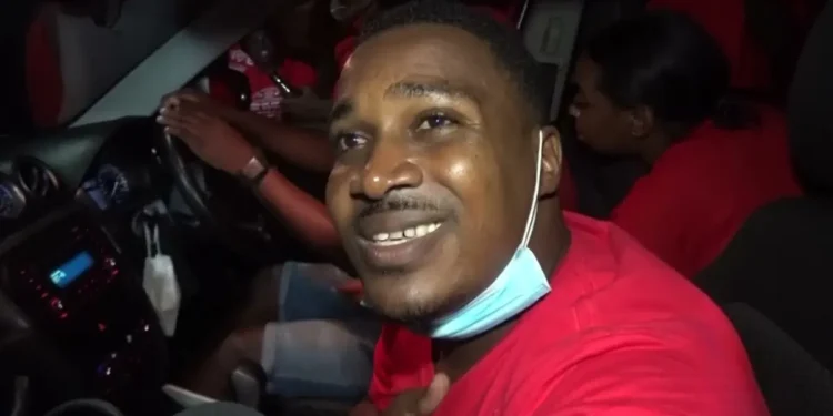 Jeremiah Norbert at a 2021 election motorcade, engaging with supporters in a red shirt and mask.