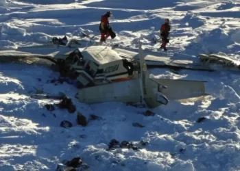 Wreckage of the Alaska plane found on sea ice near Nome, showing debris scattered across snowy terrain as U.S. Coast Guard rescue workers assess the crash site.