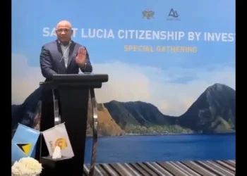 Ernest Hilaire makes shocking CIP admission at a Dubai forum, speaking at a podium with Saint Lucia and Galaxy flags, Pitons in backdrop.