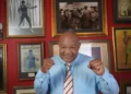 George Foreman dies at 76: boxing legend smiles in tribute photo wearing blue shirt, surrounded by historic fight memorabilia