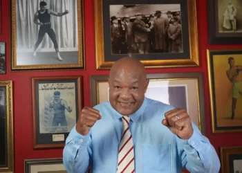 George Foreman dies at 76: boxing legend smiles in tribute photo wearing blue shirt, surrounded by historic fight memorabilia