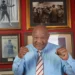 George Foreman dies at 76: boxing legend smiles in tribute photo wearing blue shirt, surrounded by historic fight memorabilia