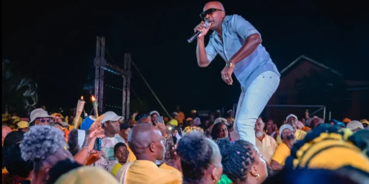 Officer Kakal performing on stage at a UWP event in Dennery, engaging with a large crowd dressed in yellow.