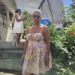 Angela Charlemagne Dies at 73, pictured in a colorful floral dress standing in a lush St Lucia garden