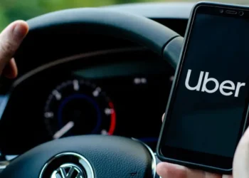 Driver holding smartphone with Uber app open while steering a Volkswagen, used in article on Uber stock Q2 earnings and $20B buyback.