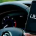 Driver holding smartphone with Uber app open while steering a Volkswagen, used in article on Uber stock Q2 earnings and $20B buyback.