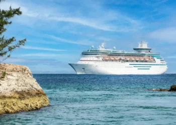 Large white cruise ship sailing in the Caribbean Sea near a rocky shoreline, illustrating concerns over Caribbean cruise ship revenue.
