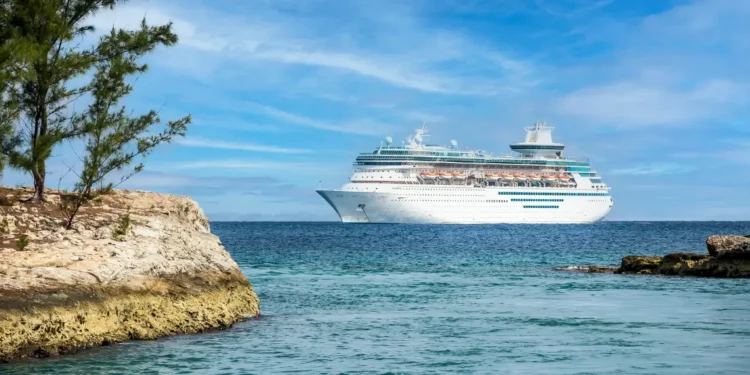 Large white cruise ship sailing in the Caribbean Sea near a rocky shoreline, illustrating concerns over Caribbean cruise ship revenue.