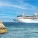 Large white cruise ship sailing in the Caribbean Sea near a rocky shoreline, illustrating concerns over Caribbean cruise ship revenue.