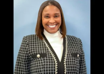 Teri Helenese urges sustainable tourism growth in a professional portrait wearing a black-and-white blazer against a light blue background.