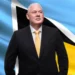 Allen Chastanet COVID-19 leadership depicted as he stands confidently before the Saint Lucian flag in a suit and yellow tie