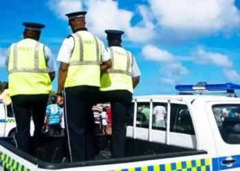 Police officers standing in a patrol vehicle during a daytime operation related to Customs employees arrested in St Lucia.