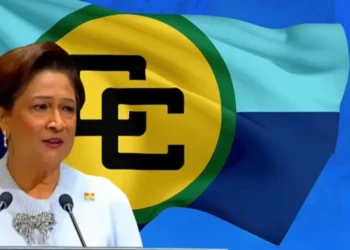 Kamla Persad-Bissessar speaking at a podium with the Caricom flag behind her as she says Caricom dysfunctional