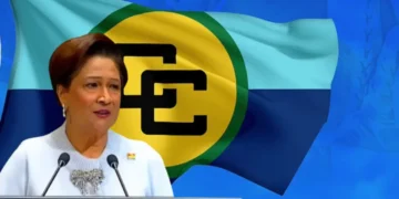 Kamla Persad-Bissessar speaking at a podium with the Caricom flag behind her as she says Caricom dysfunctional