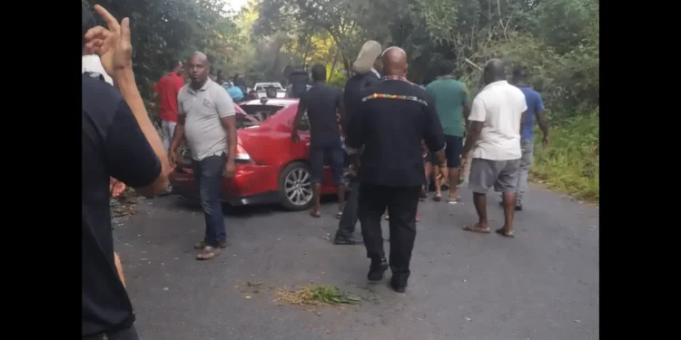 Serious accident at Ladera Gap as bystanders gather around a damaged red vehicle following a traffic crash in Soufrière