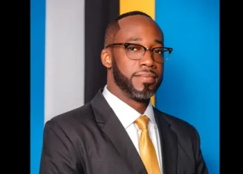 Elisha Norbert wearing a suit and gold tie in a formal portrait against a blue background