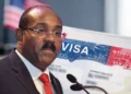 Gaston Browne urges US visa caution in a composite image showing the prime minister beside a close-up of a US visa page with a blurred American flag in the background.