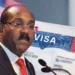 Gaston Browne urges US visa caution in a composite image showing the prime minister beside a close-up of a US visa page with a blurred American flag in the background.