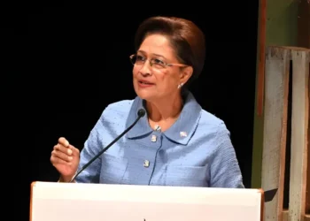 Prime Minister Kamla Persad-Bissessar speaks at a podium as Trinidad Declares State of Emergency