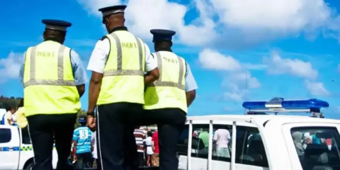 Three RSLPF officers in high-visibility vests beside a marked police vehicle during the Anse La Raye arrest operation.