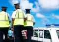 Three RSLPF officers in high-visibility vests beside a marked police vehicle during the Anse La Raye arrest operation.