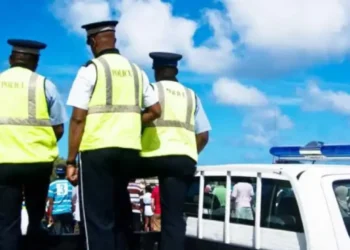 Three RSLPF officers in high-visibility vests beside a marked police vehicle during the Anse La Raye arrest operation.